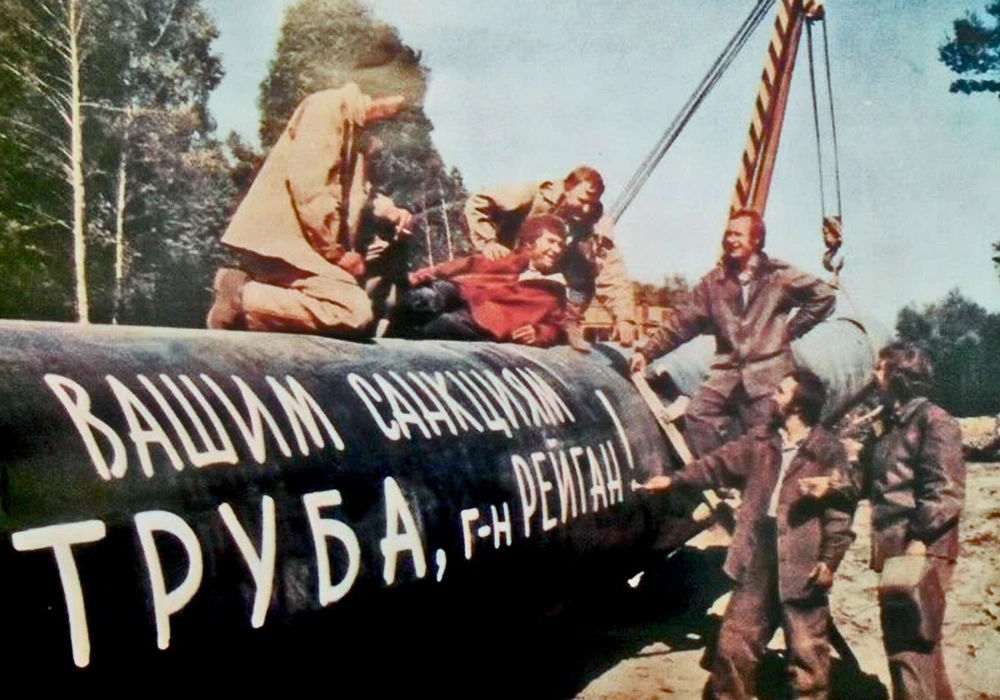 Soviet pipeline workers in 1982 beside a pipe painted with the slogan: Your sanctions are done for, Mr. Reagan!